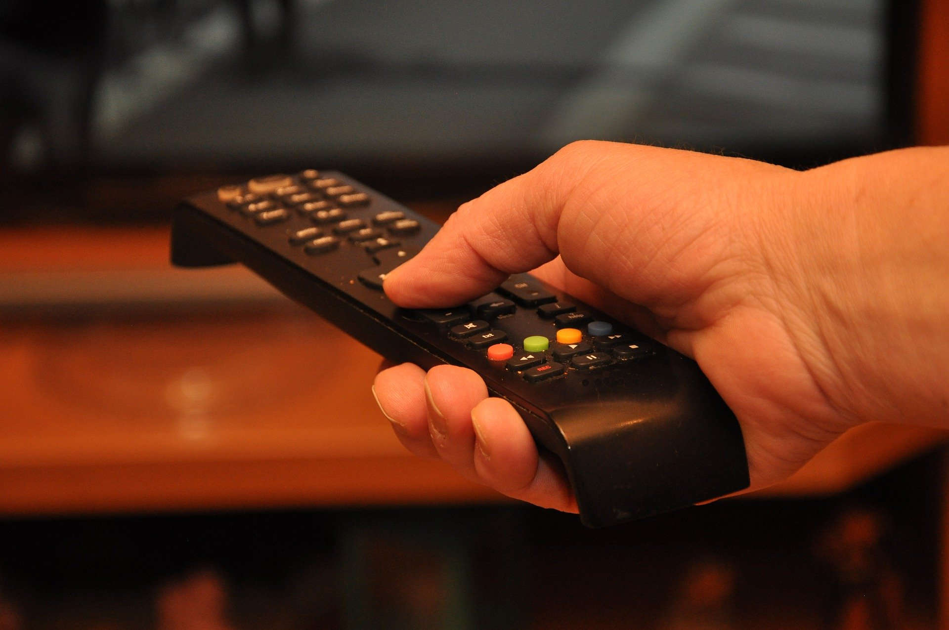 Primer plano de una mano con un mando a distancia apuntando a una televisión