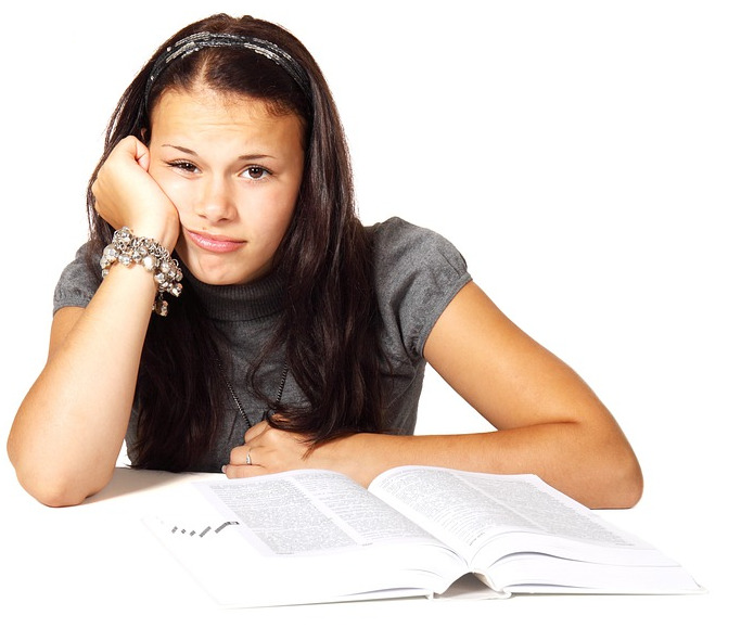 Adolescente (chica) con un libro delante mirando a la cámara con cara de preocupación