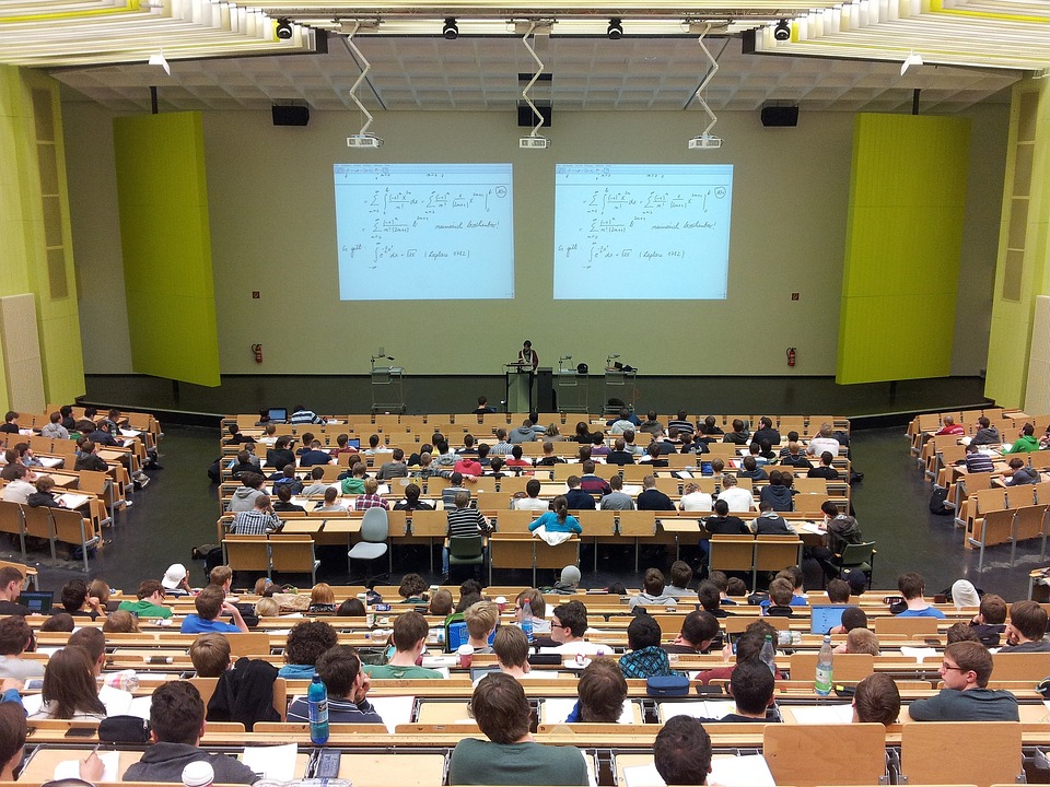 Aula magna de una universidad, desde arriba, con alumnos y un profesor dando una clase