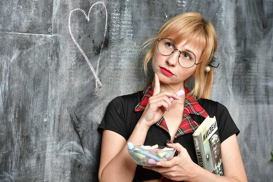 Mujer j&oacute;ven delante de una pizarra con gesto pensativo y en la mano un recipiente con tizas